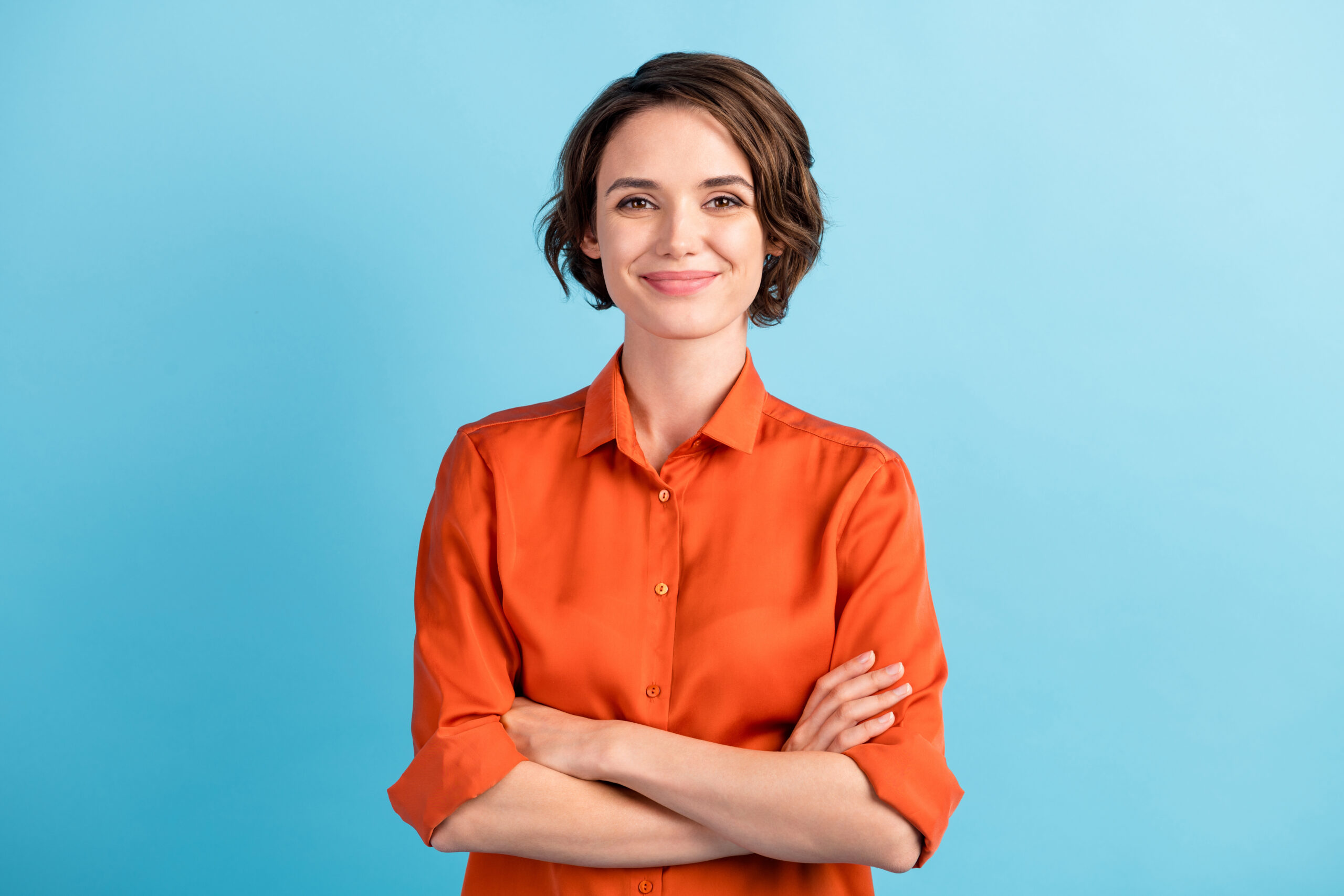 Photo of attractive charming lady cute bobbed hairdo arms crossed, self-confident person worker friendly smile good mood wear orange office shirt isolated blue color background
